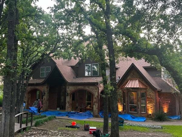Stone and timber home in Weatherford, TX with tarps protecting the landscaping during a roof replacement