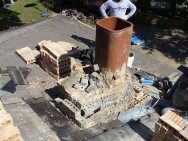 Chimney stripped down to its base with replacement brick stacked on the roof ready to go back