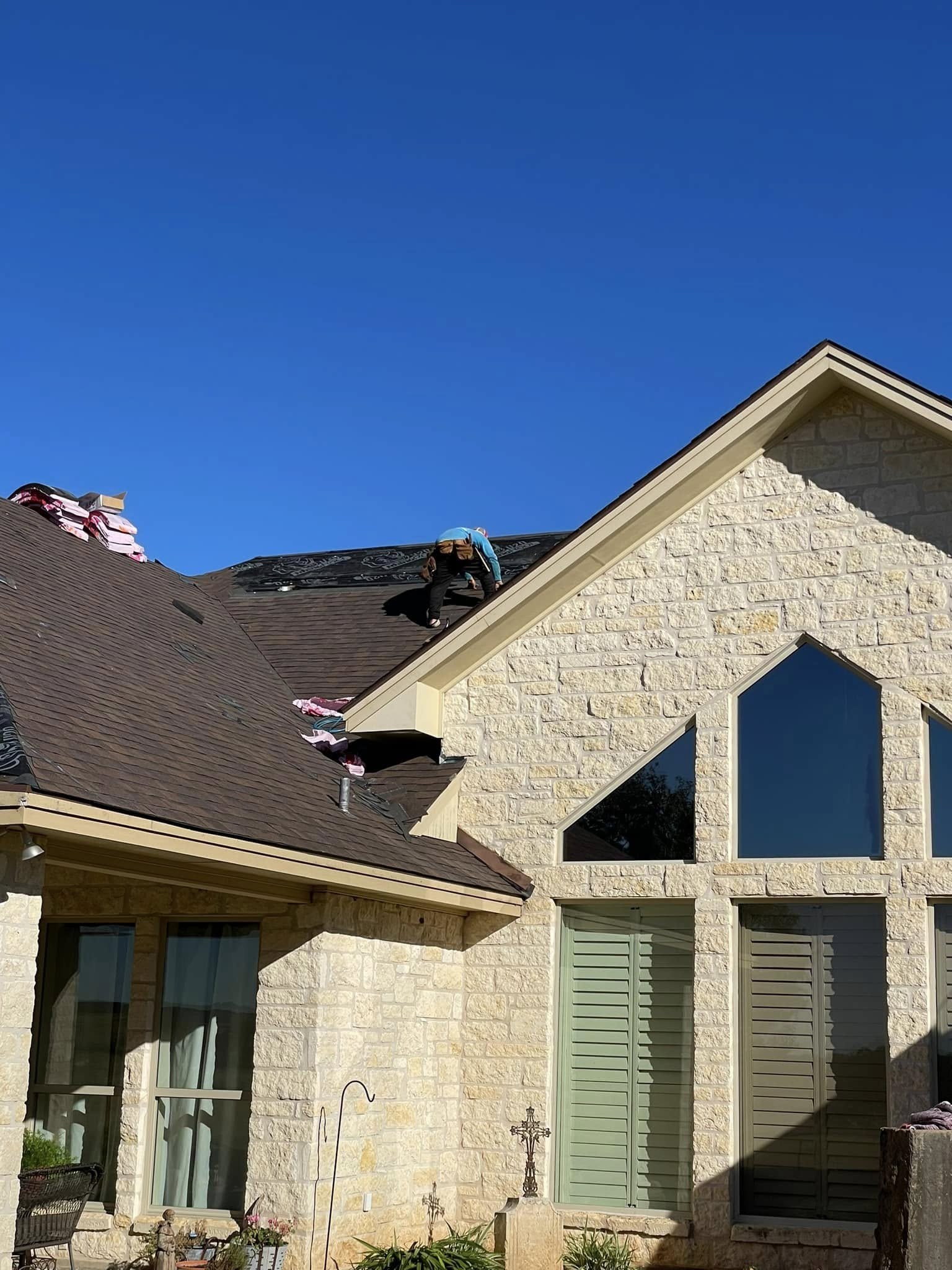 Roof tear-off underway on a stone home, with the old shingles stripped back to the decking